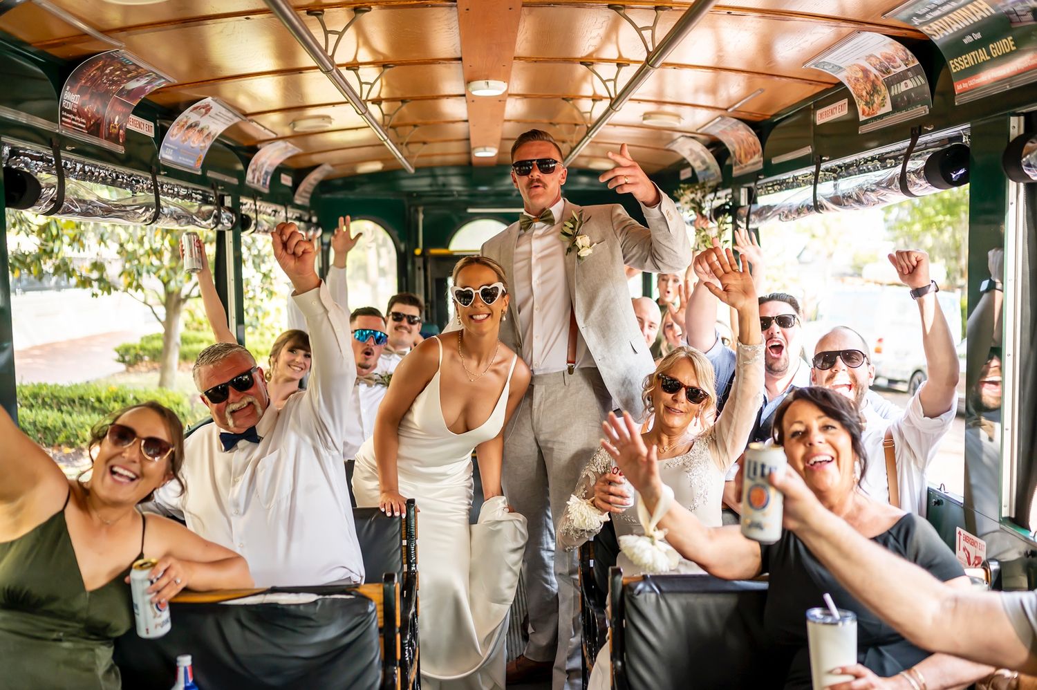 Wedding party celebrates while riding in a vintage trolley car with wood paneled ceiling.