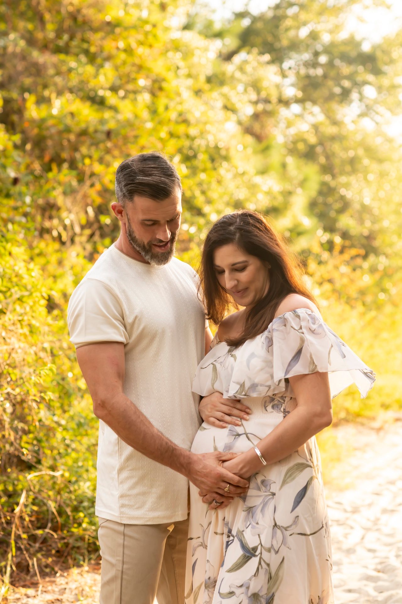 A couple shares an intimate moment outdoors in golden sunlight as they lovingly embrace a pregnant belly.