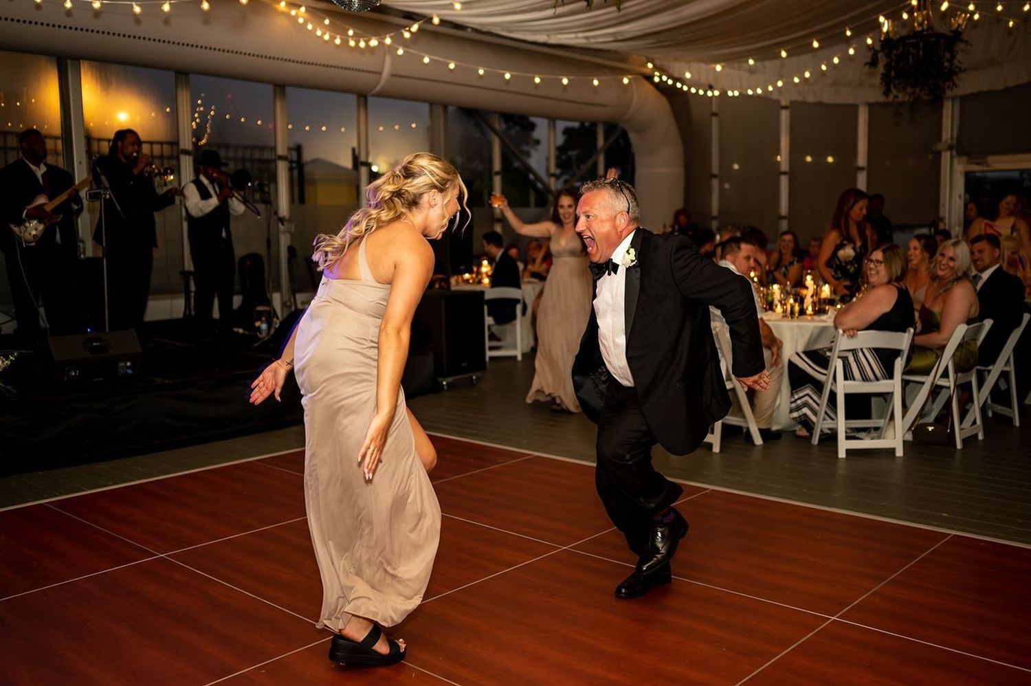 Couple dances joyfully together on a dance floor under twinkling lights at an evening reception.
