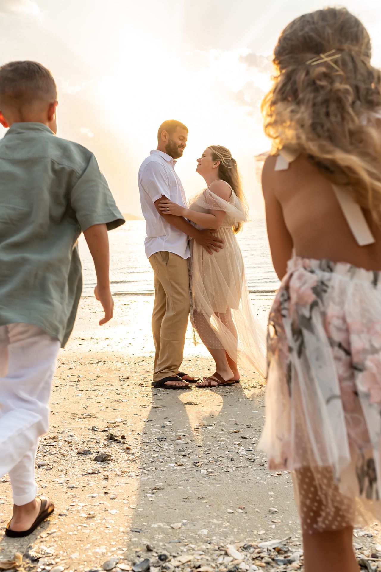 Multiple people in casual attire walk along a sandy beach at sunset with soft golden sunlight illuminating the scene.