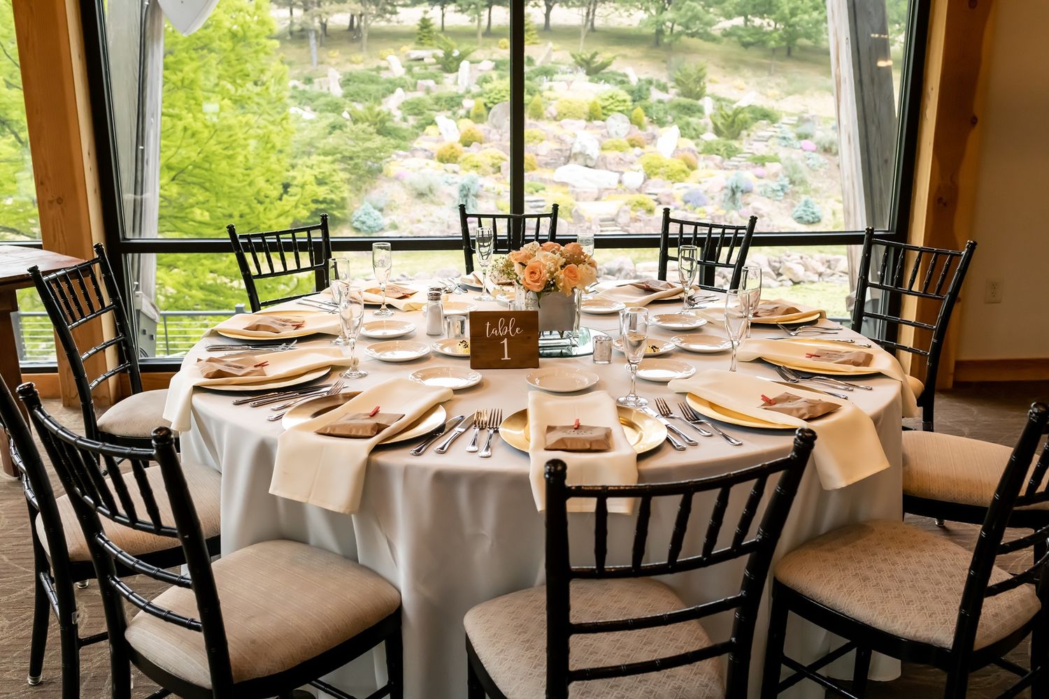 Elegant wedding reception tables set with white linens and rustic chairs in a bright window-filled venue.