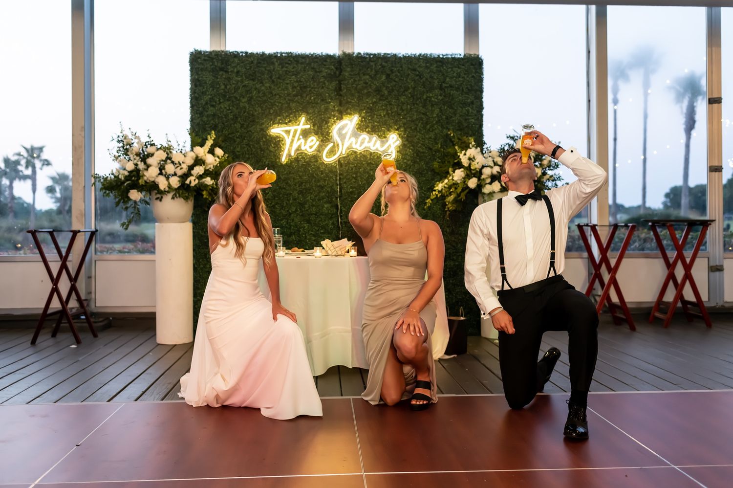A couple in wedding attire sits together on bistro chairs during an evening reception on an outdoor deck.
