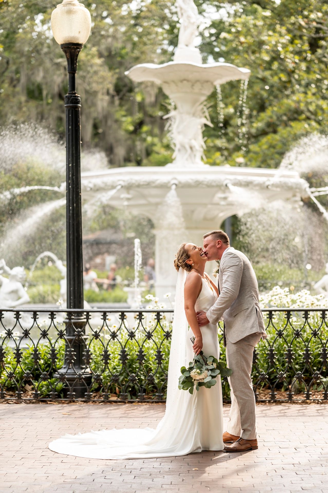 A bride and groom kiss in front of the fountain at Forsyth Park.
