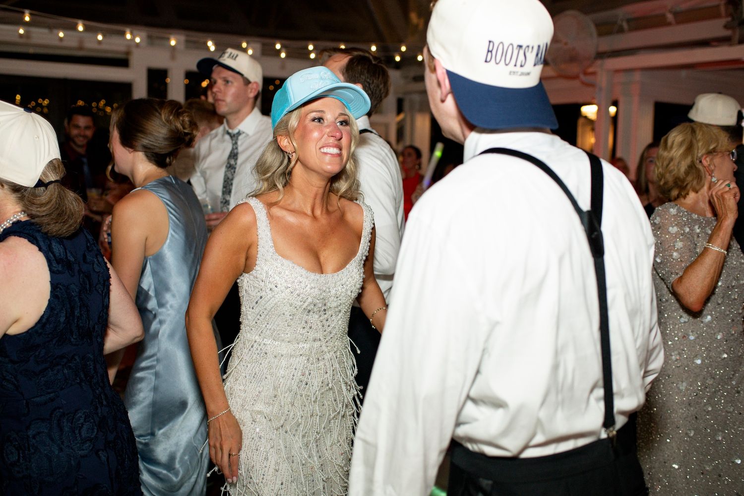 Couple dancing at a wedding reception, woman in sequin dress and blue cap, man in white shirt with suspenders.