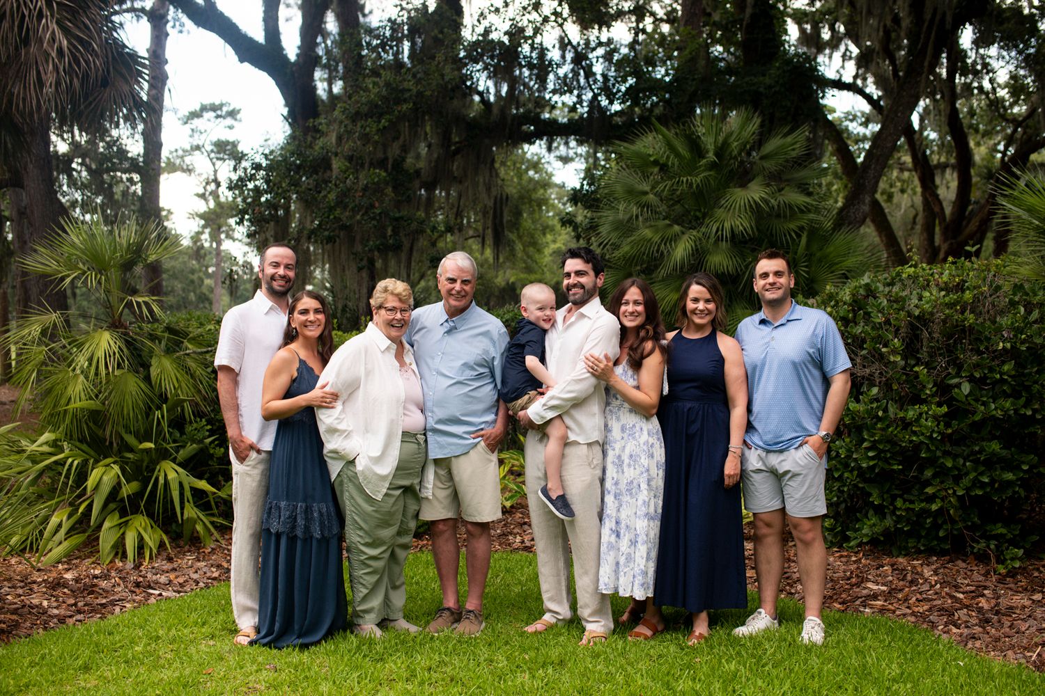 Group of people in casual attire standing together outdoors in a garden setting with lush greenery in the background.