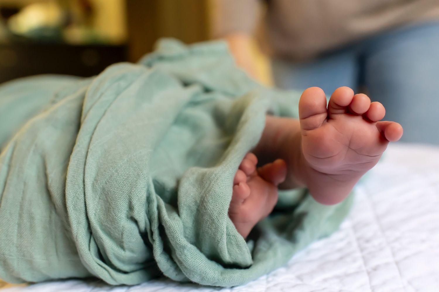 Close-up sequence of newborn baby feet wrapped in mint green blanket shows gradual unwrapping motion.