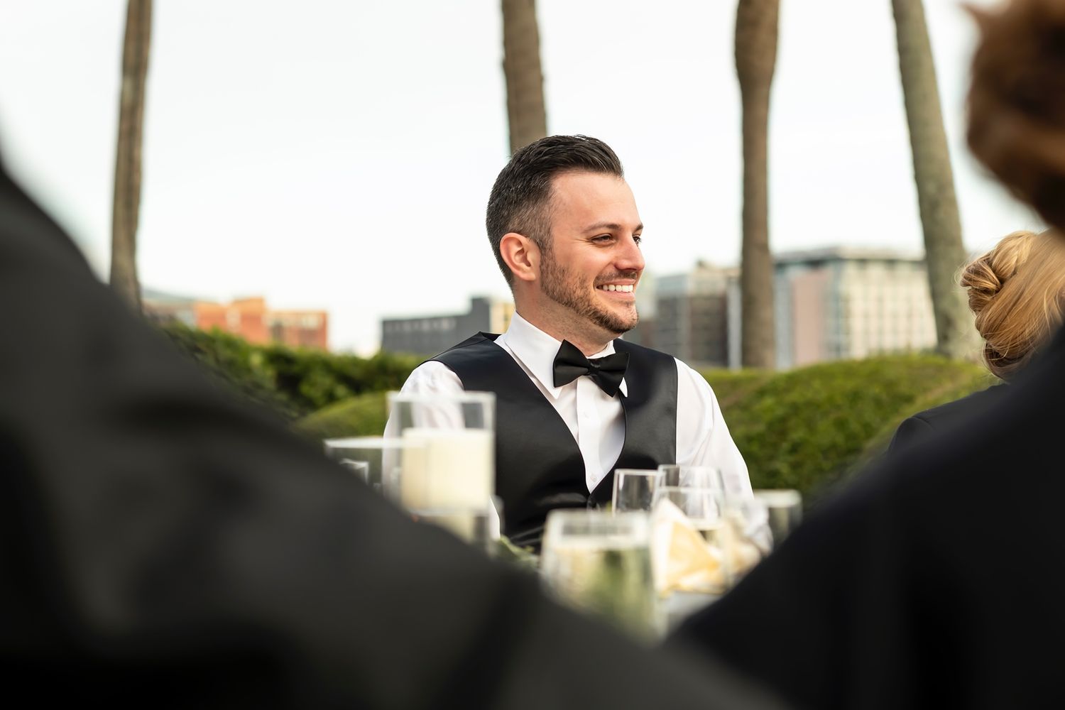 A server in formal attire smiles while working at an outdoor catering event during daytime.