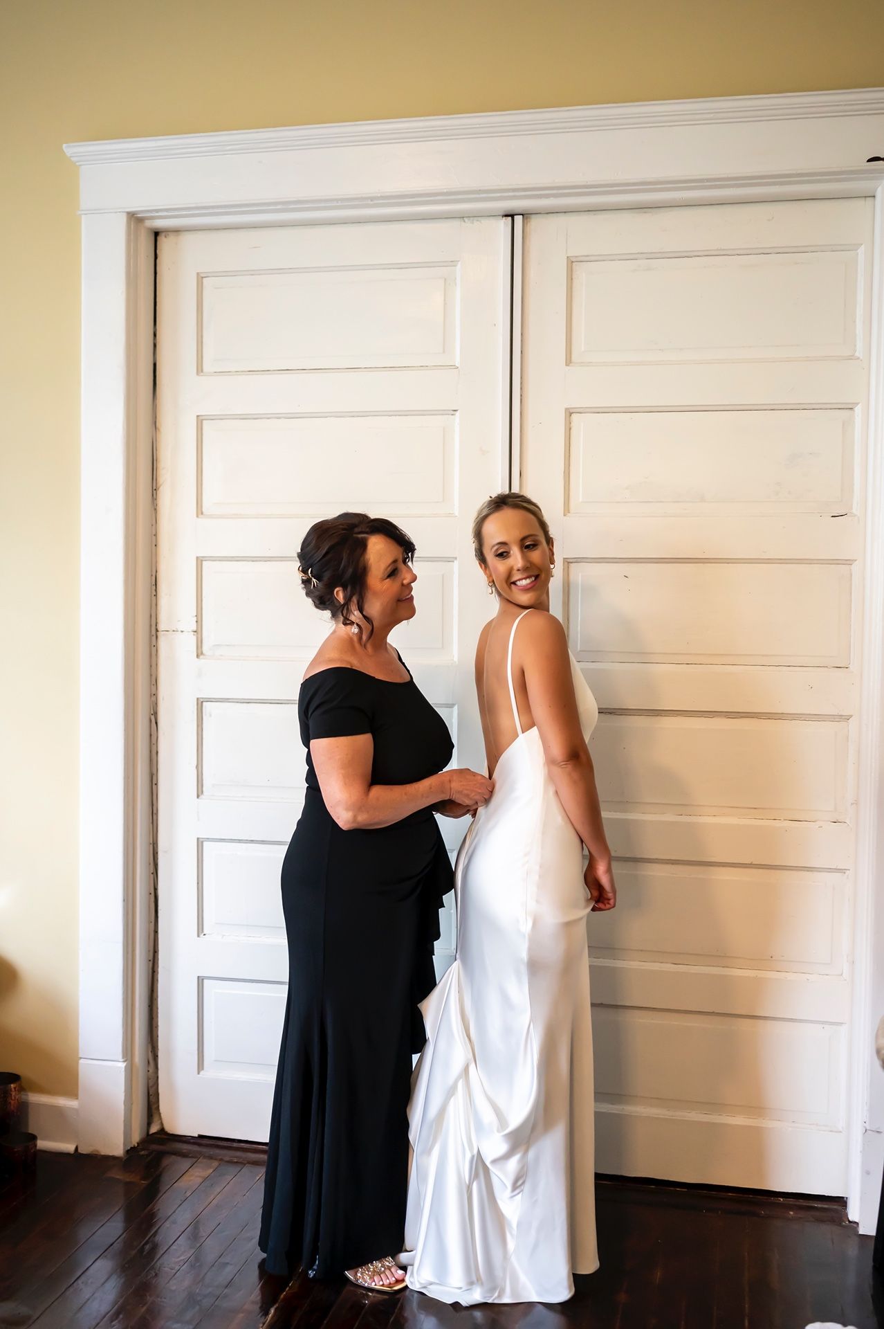 Two people share a joyful moment in formal attire against white double doors on hardwood floors.