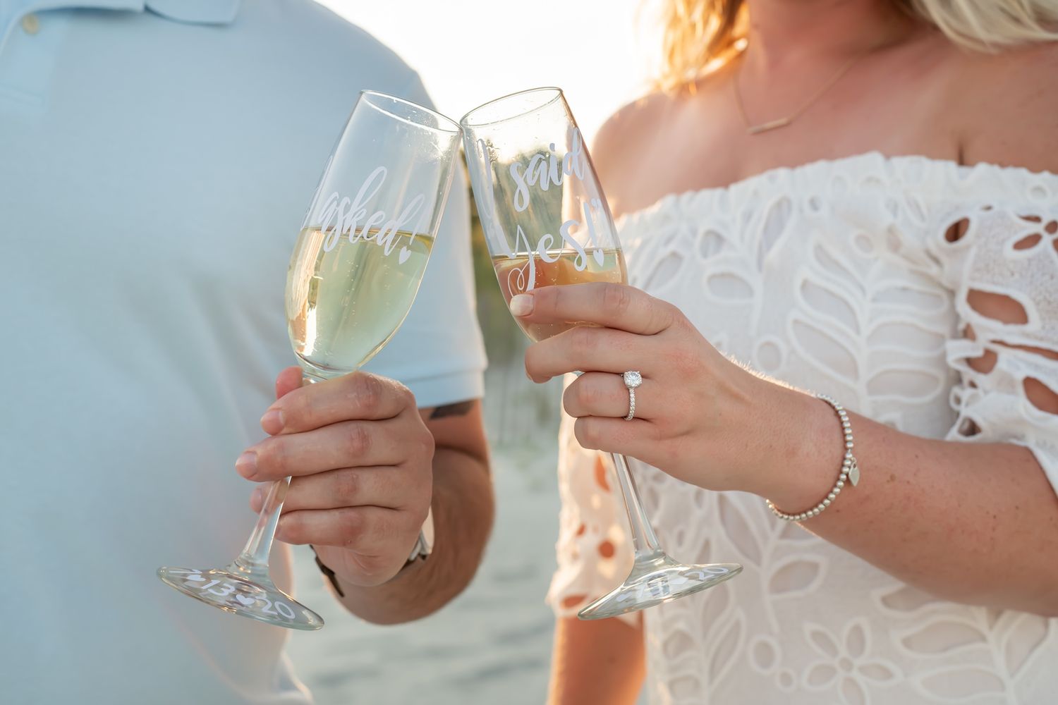 Two champagne flutes clinking together in a celebratory toast at a wedding with bride in white lace dress.