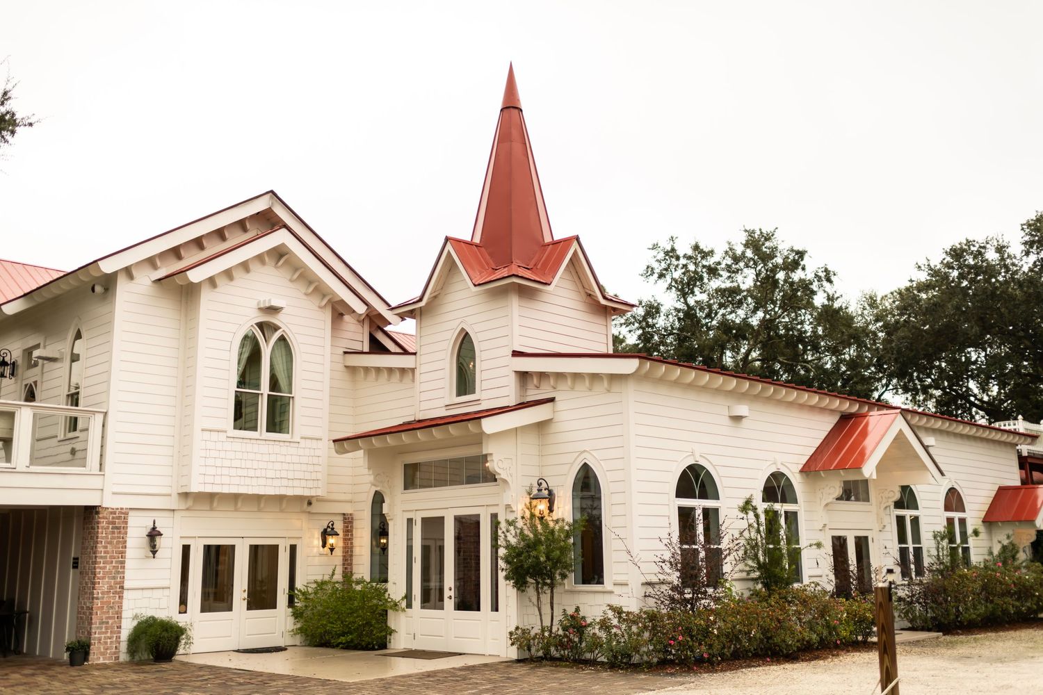 White chapel building with gothic arched windows and multiple red-peaked steeples surrounded by landscaping.