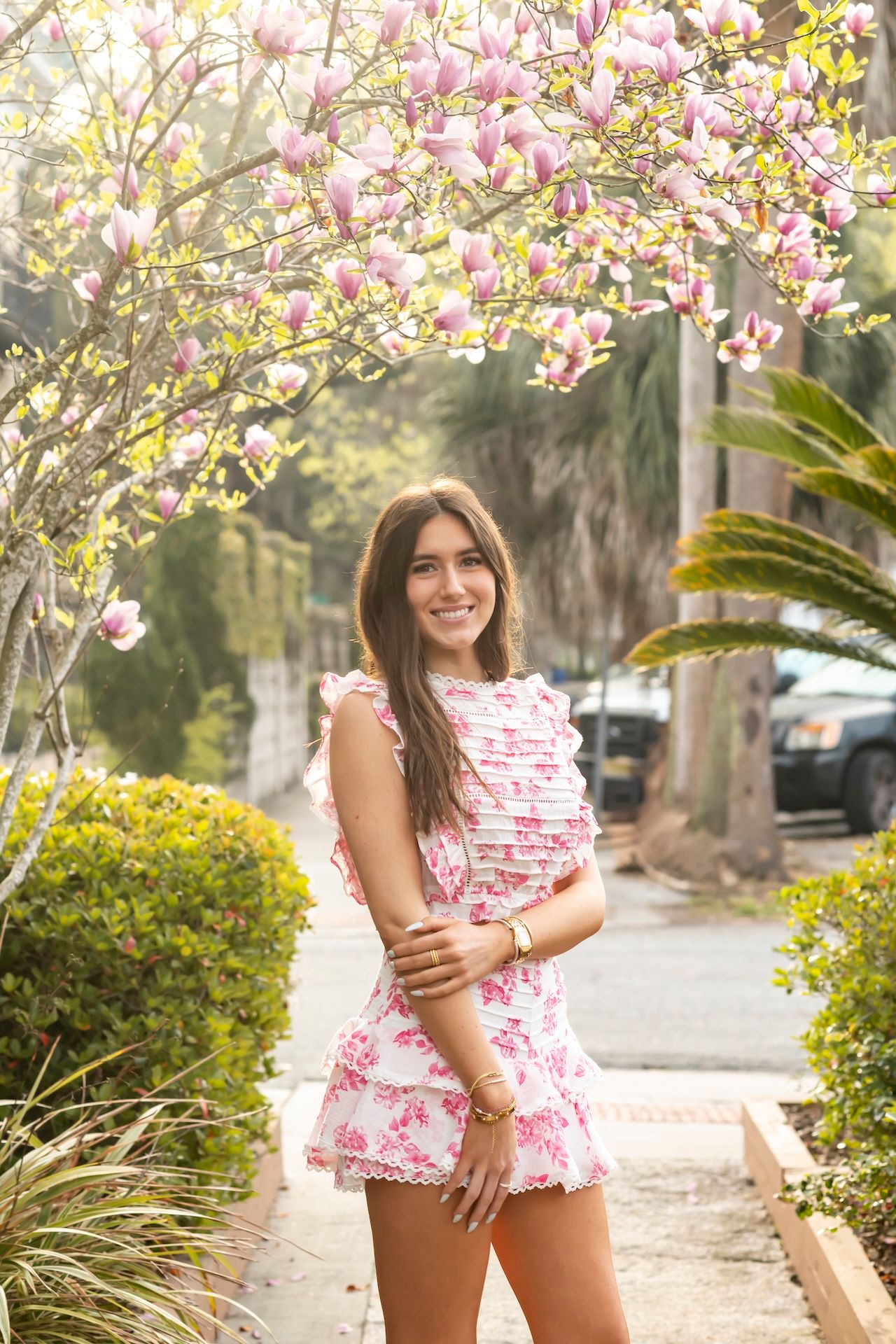 A feminine pink floral two-piece outfit styled against blooming magnolia trees in a garden setting.