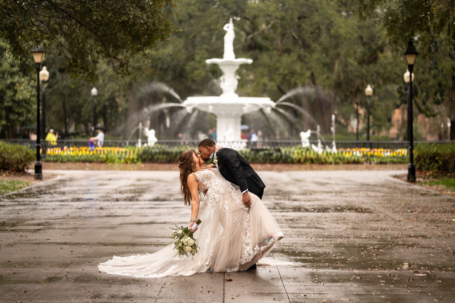 Romantic wedding couple shares an intimate moment in the rain near a beautiful fountain at Forsyth Park in Savannah Georgia.