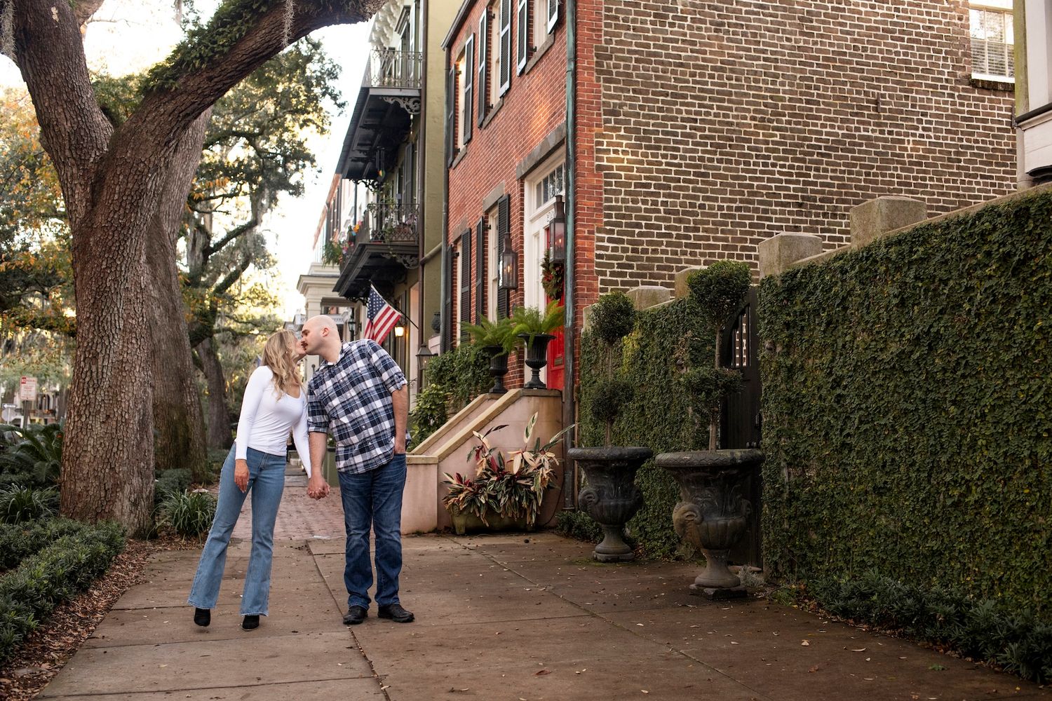People walking along a brick-lined path with historic brownstone buildings and lush ivy walls in a charming urban setting.