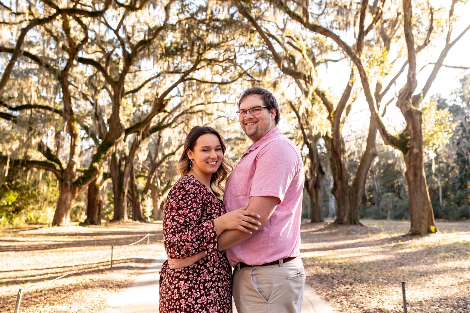 Two people share an affectionate moment among sunlit oak trees during a romantic outdoor photo session.