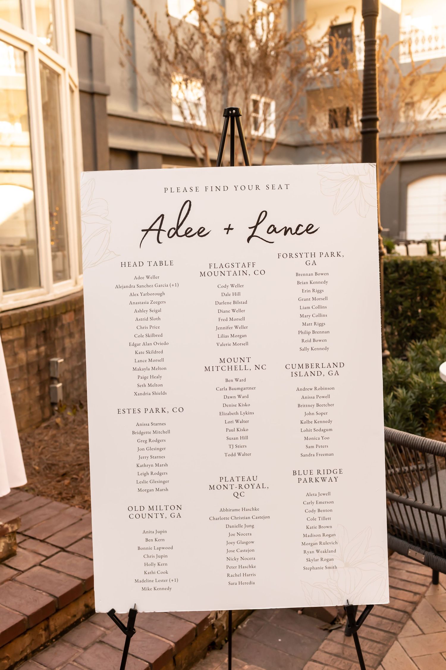 Elegant wedding seating chart displays guest names on white paper signs mounted against a rustic wood backdrop.