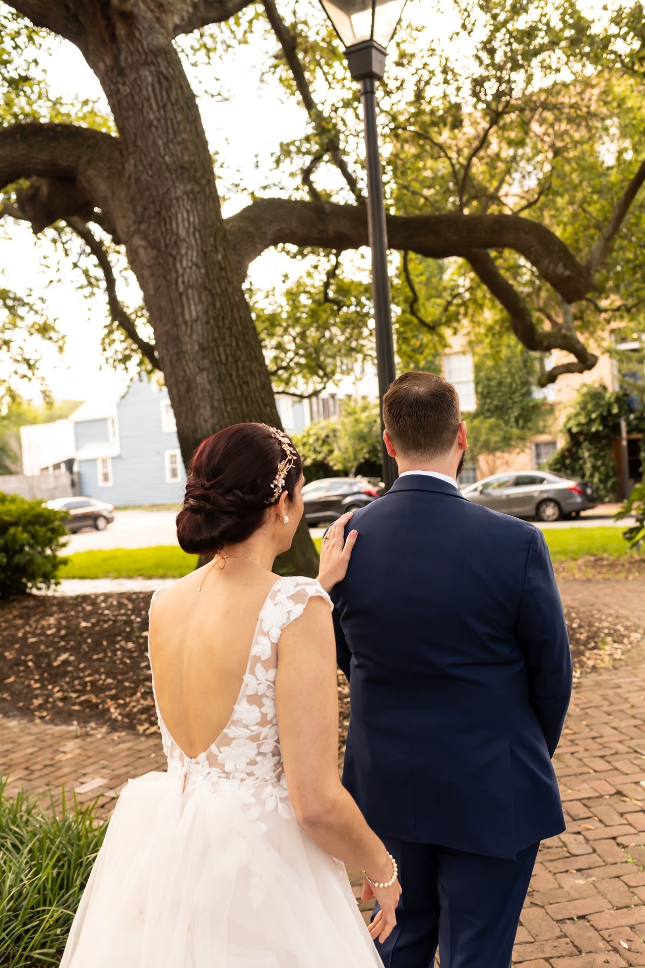 Couple walking together on a brick pathway surrounded by trees and greenery in elegant wedding attire.