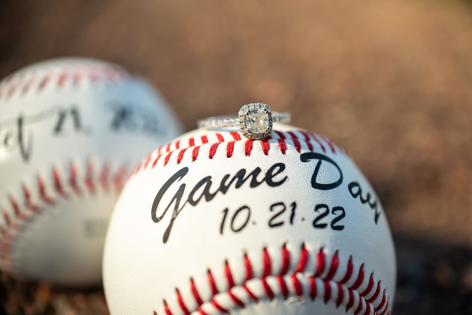An engagement ring rests on a signed baseball with 'Game Day' written and dated 10.21.22.