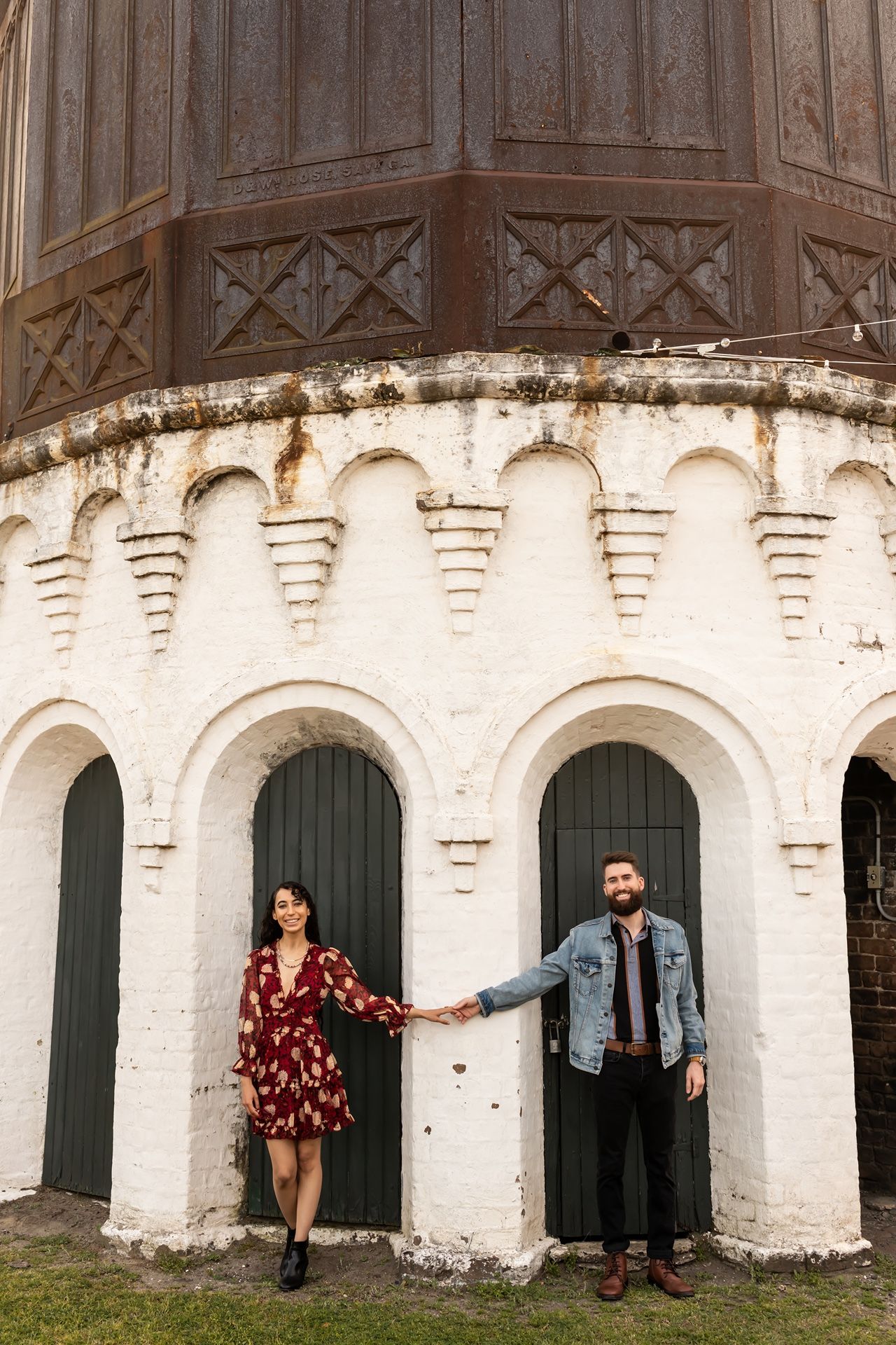 Couple stands at base of ornate church tower with white stone arches and decorative architectural details.