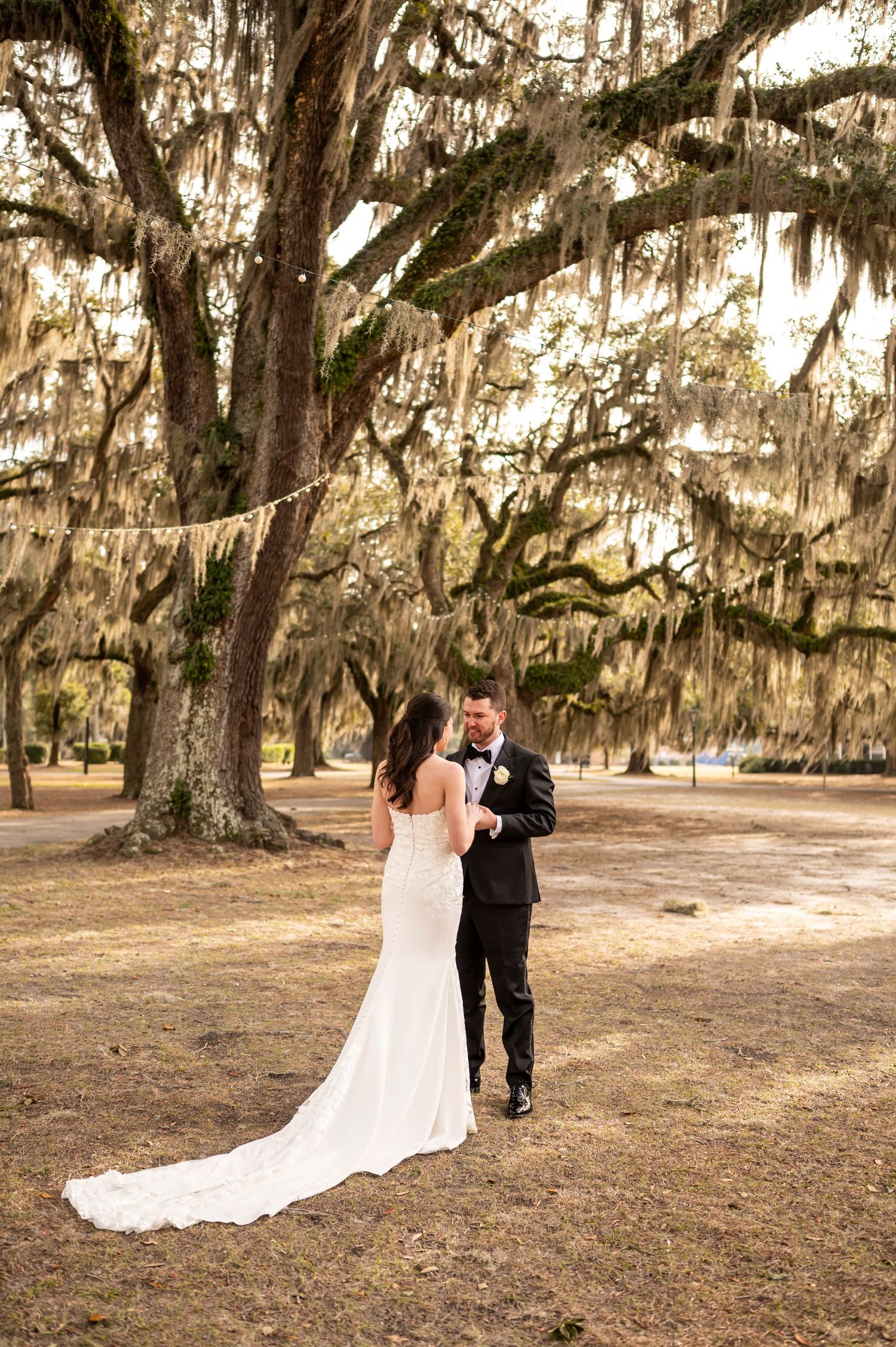 Couple poses under majestic Spanish moss-covered oak trees in romantic southern wedding ceremony setting.
