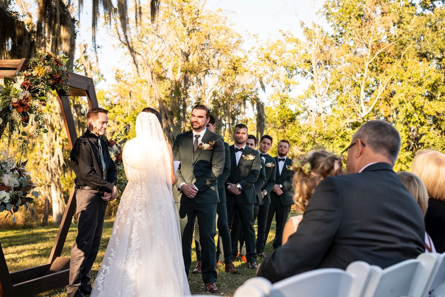 Newlyweds celebrate at outdoor wedding ceremony with guests smiling in golden autumn sunlight.