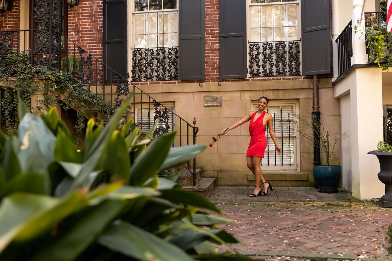 Someone in a vibrant red dress twirls elegantly on a historic brick courtyard with ornate windows and lush greenery.