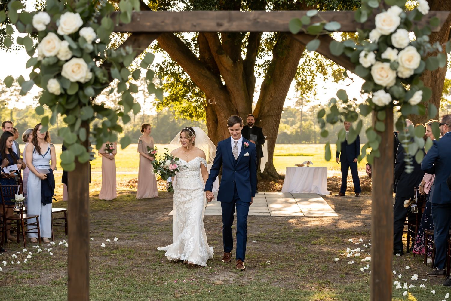 Two newlyweds share a romantic moment under a tree lined path as golden sunlight filters through the leaves.