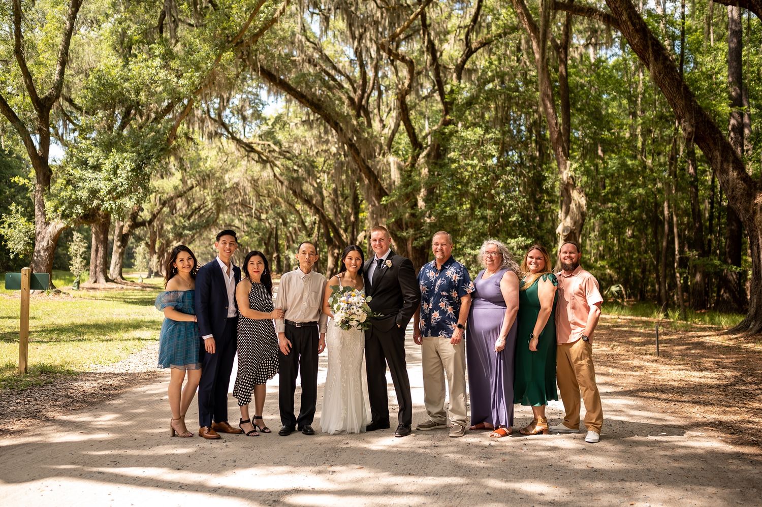 Wedding party gathered in a scenic tree-lined pathway surrounded by lush greenery and natural light.