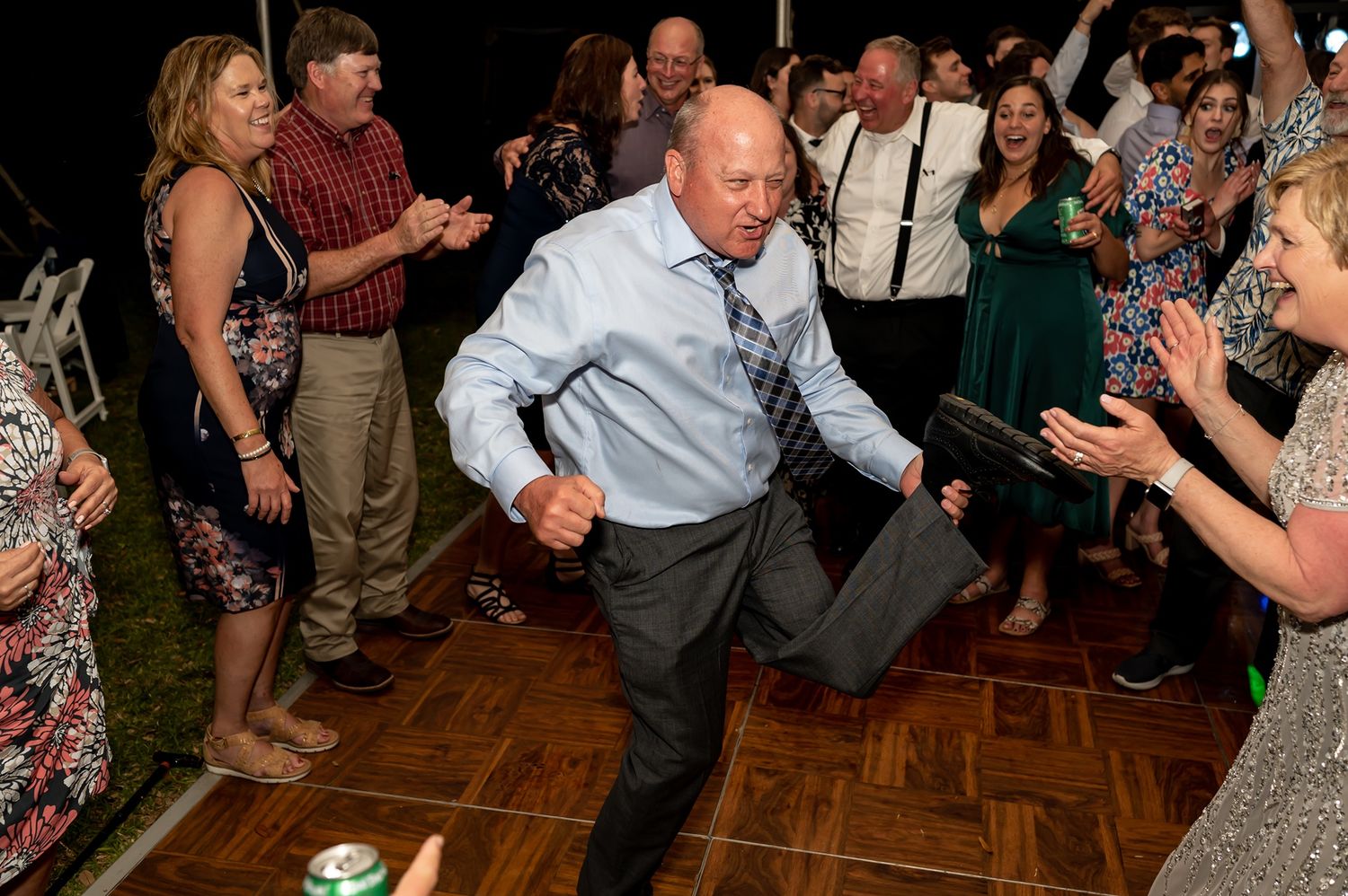 A guest shows off energetic dance moves on a wooden floor at an outdoor wedding reception.