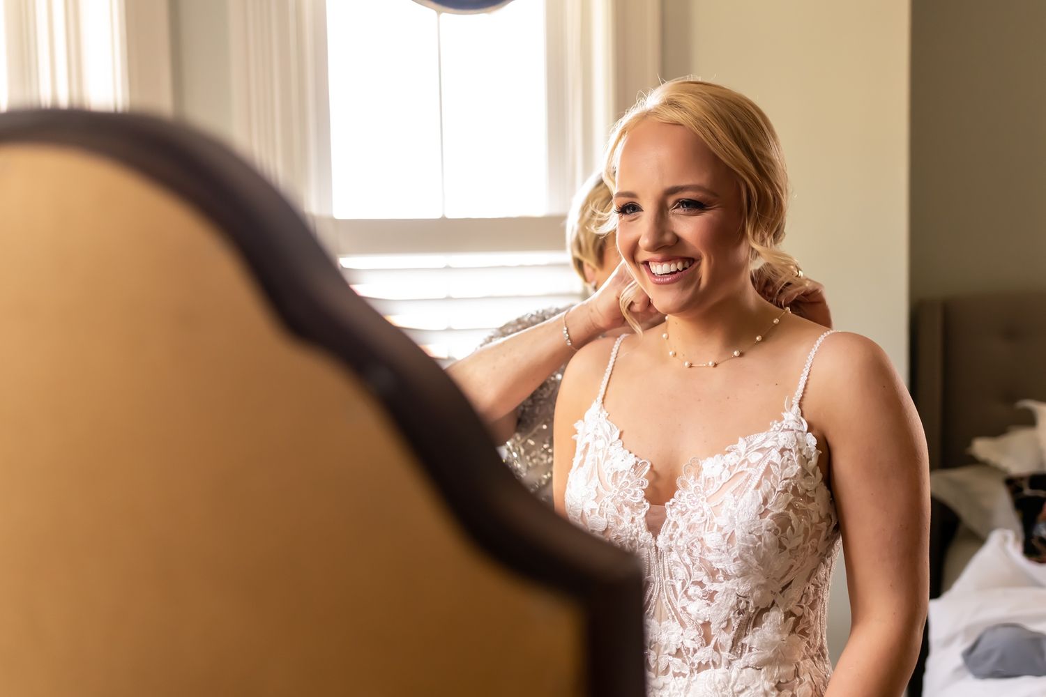 Natural candid moment of someone in an elegant lace wedding dress smiling while sitting near a window.