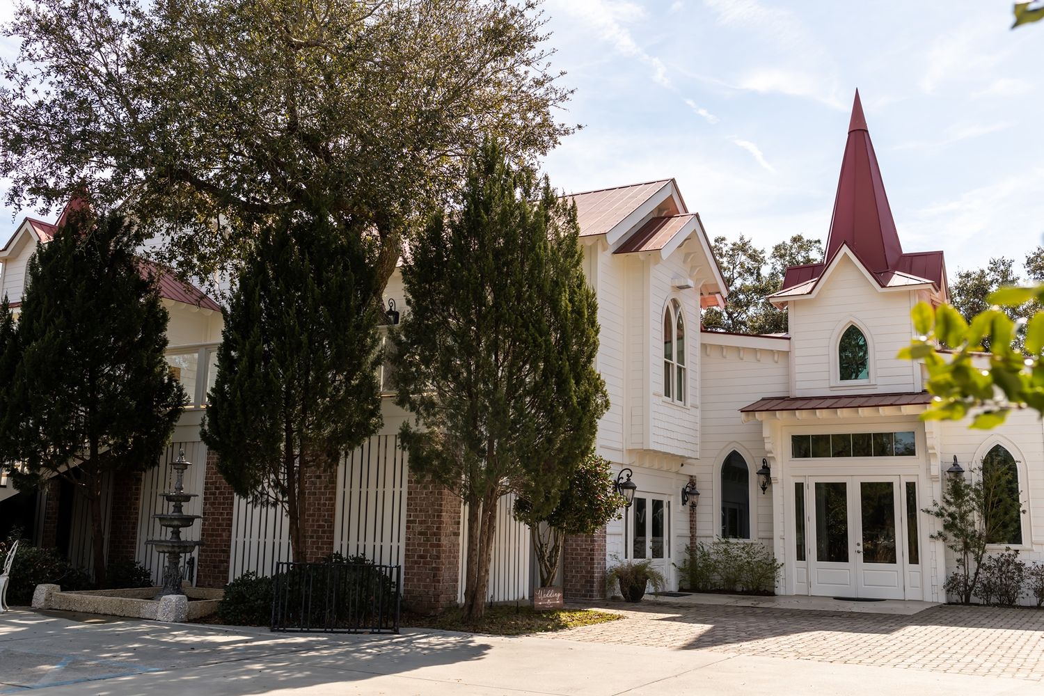 White church building with red spire and tall trees in front on a sunny day.