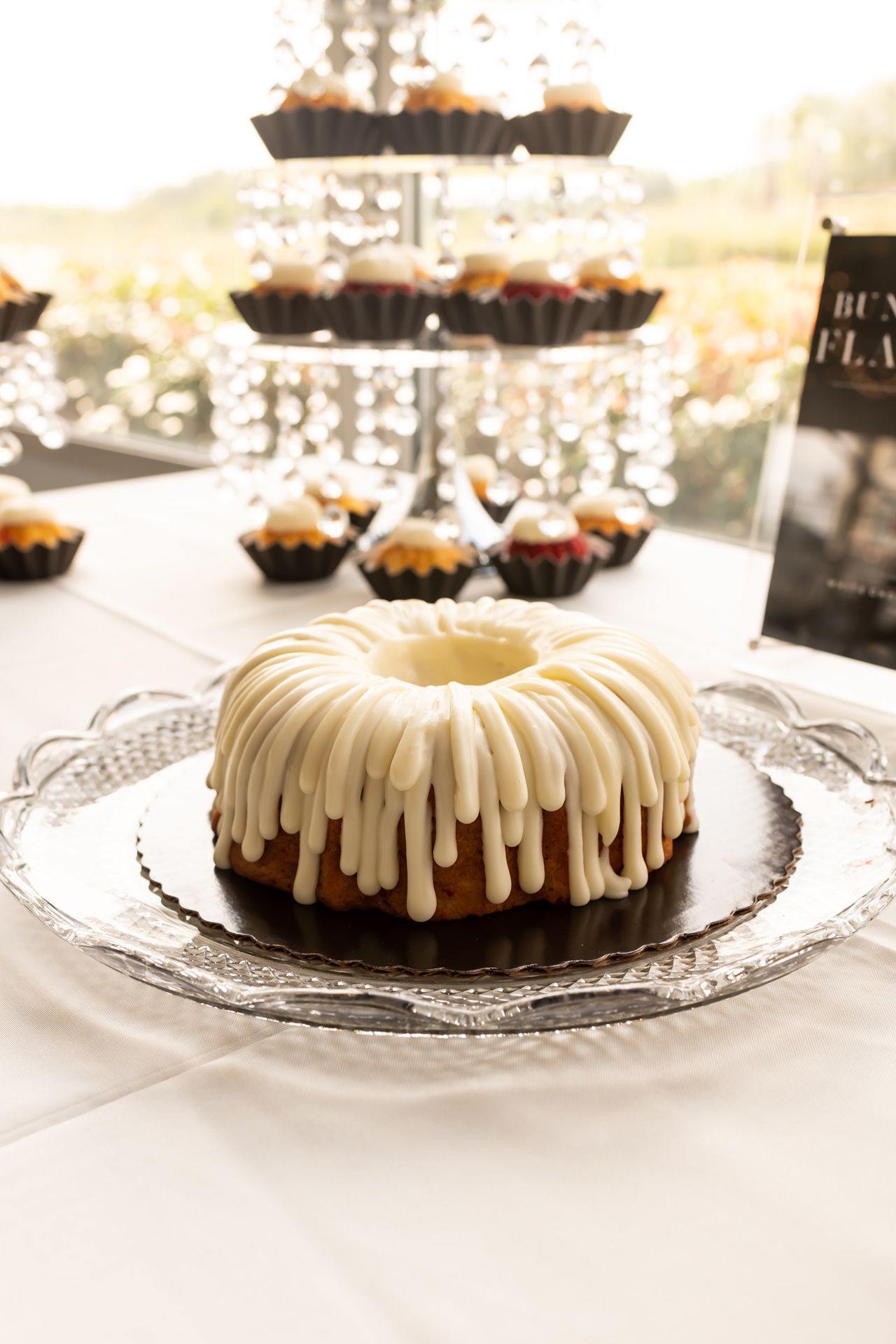 A glazed vanilla bundt cake with white icing drizzle displayed on an elegant silver serving platter.