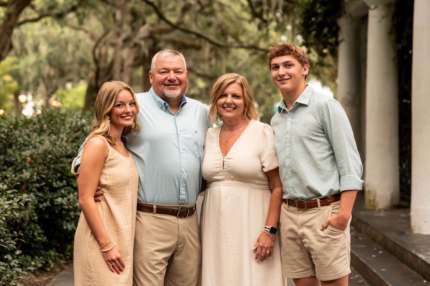 A group poses together for a formal outdoor portrait in front of lush greenery.
