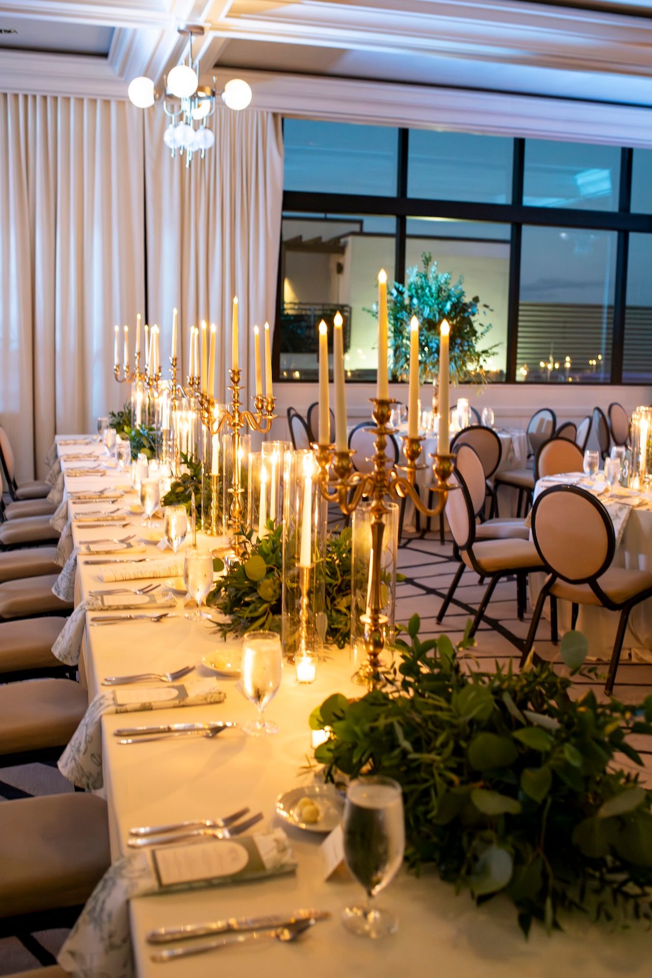 Elegant wedding reception tables set with white linens, candelabras, and greenery garlands in an upscale dining room.
