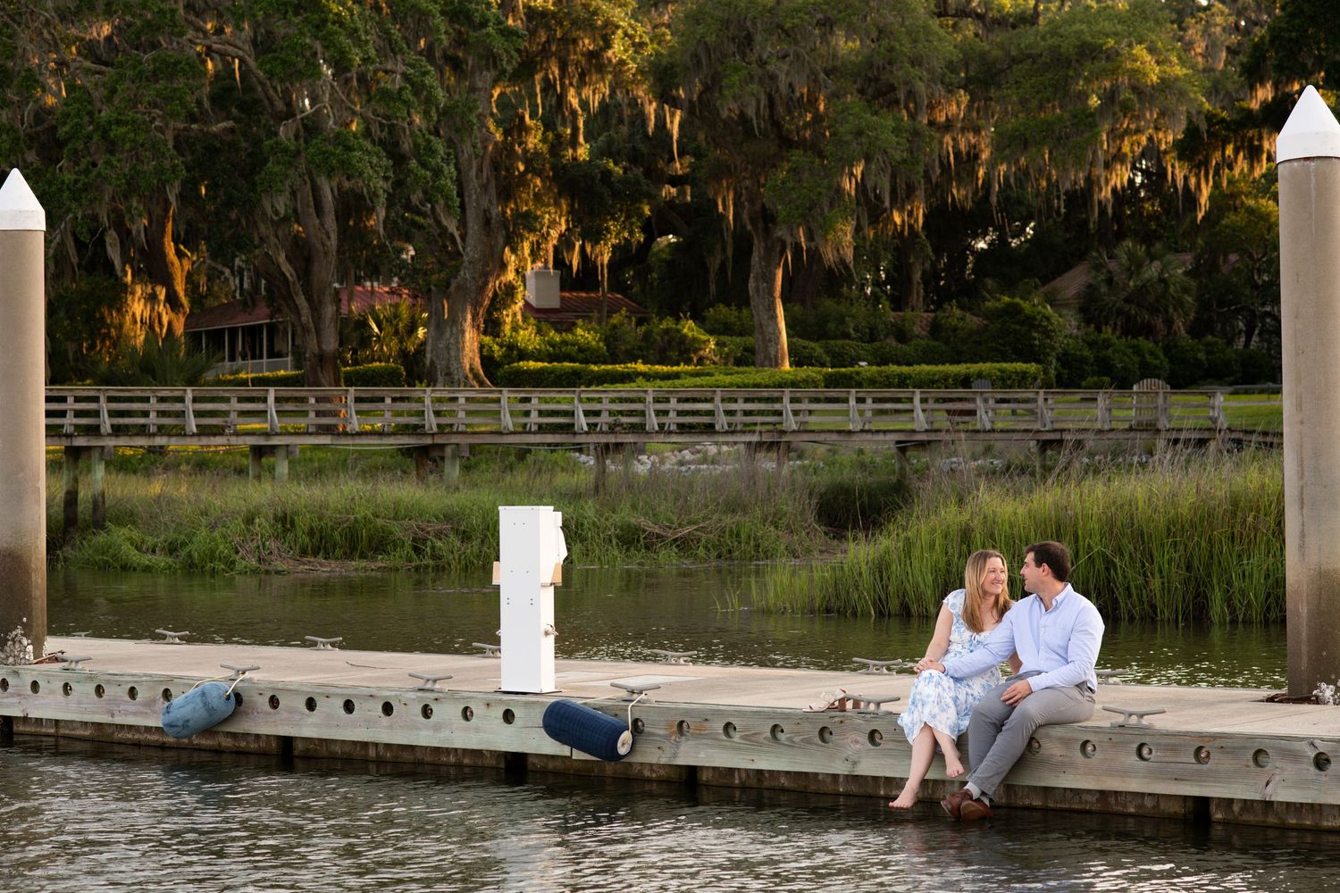Couple sits on white dock overlooking tranquil lake during golden sunset hour.