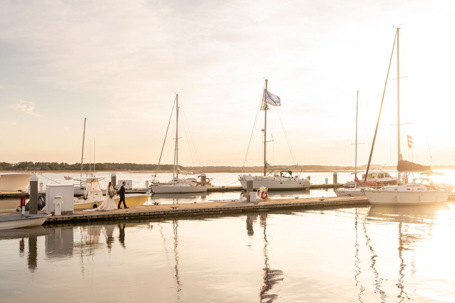 Panoramic view of boats docked at marina during golden sunset with calm water reflections.