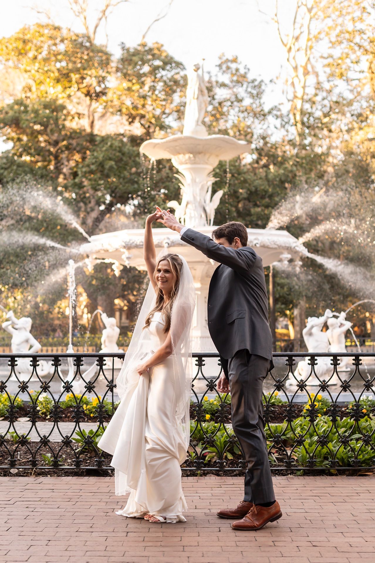 A series of photos showing wedding couple playfully dodging water sprays from a fountain in a garden at sunset.