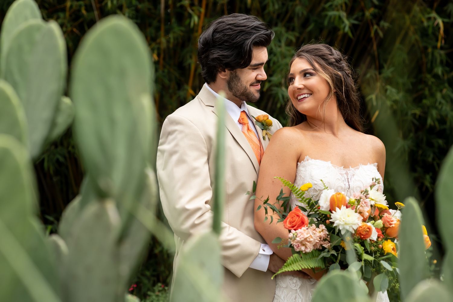 A bride and groom share a candid moment together in a garden setting with cacti in the foreground.