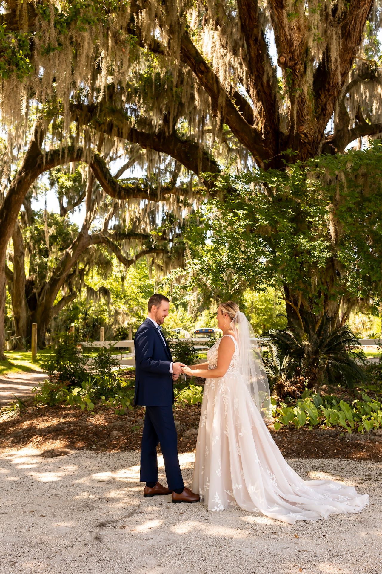 A couple shares a romantic moment under Spanish moss-draped oak trees in a beautiful Southern garden setting.