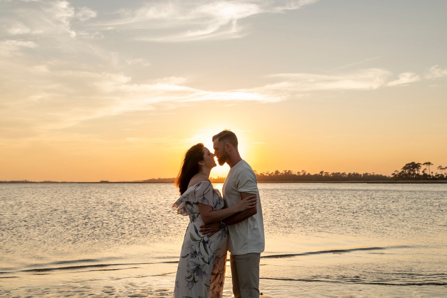 Silhouette of a couple embracing at sunset on a beach with calm water and golden sky in the background.