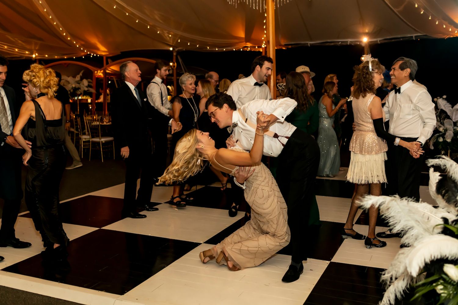 A lively reception dance floor with guests dancing under warm string lights during an evening wedding celebration.