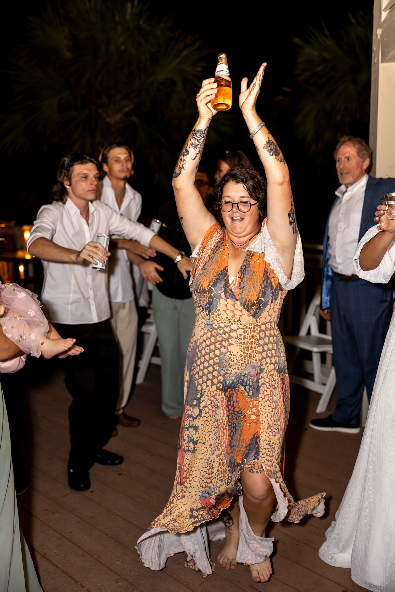 Celebratory party guest in patterned dress raises a drink bottle while dancing at a festive evening event.