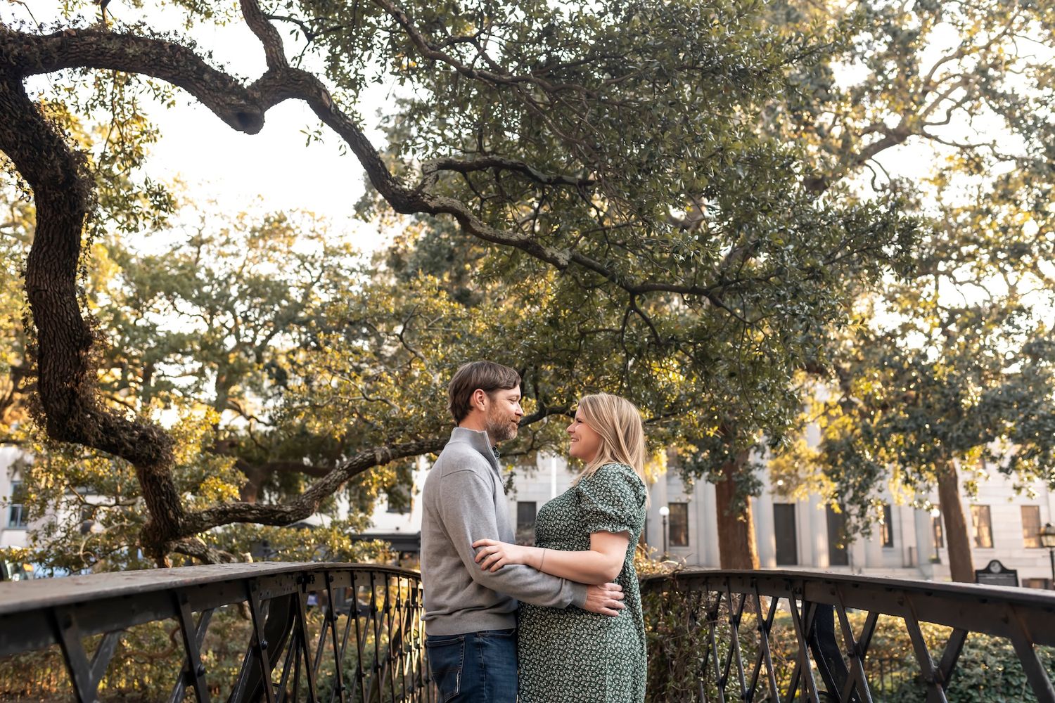 A romantic couple embraces under towering oak trees at sunset creating a dreamy silhouette effect.