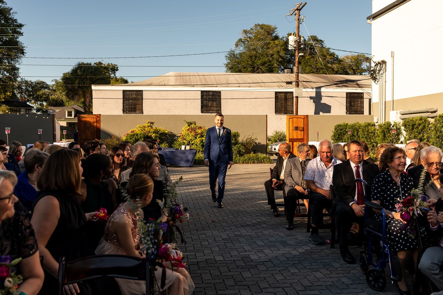 Wedding ceremony held outdoors on stone patio with guests seated on chairs during golden hour.
