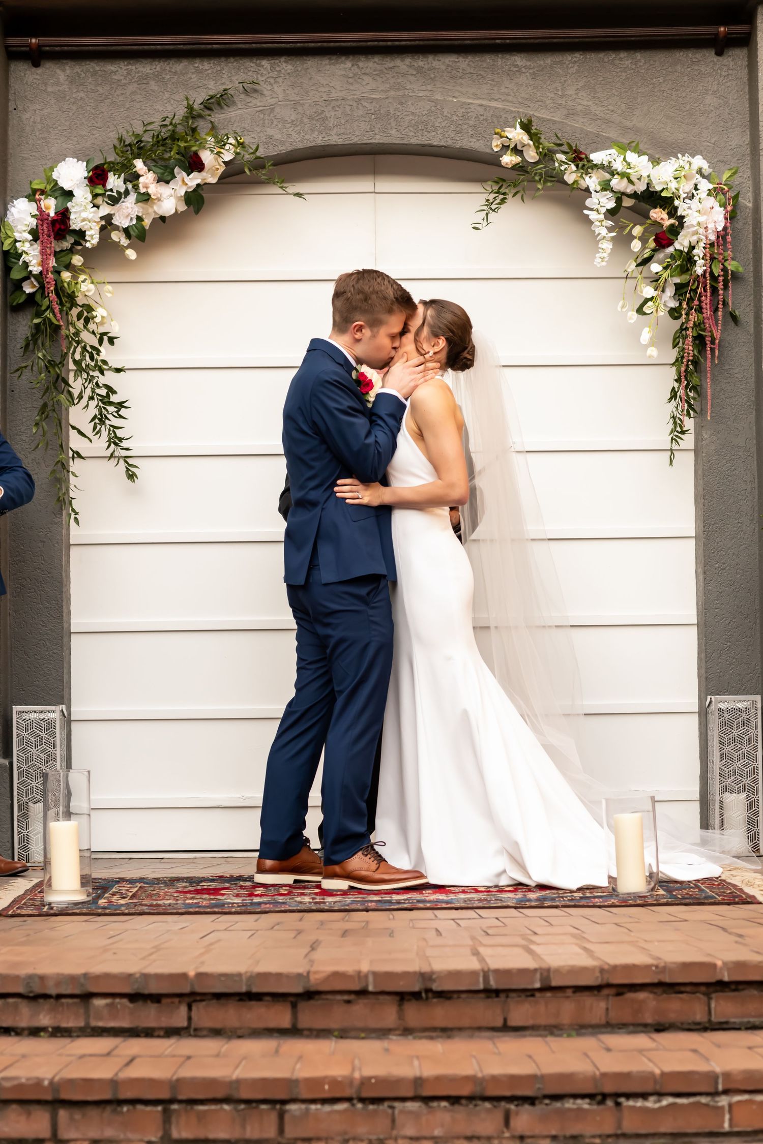 A sequence of photos showing a bride and groom sharing a progressive first kiss on a brick ledge decorated with floral garlands.