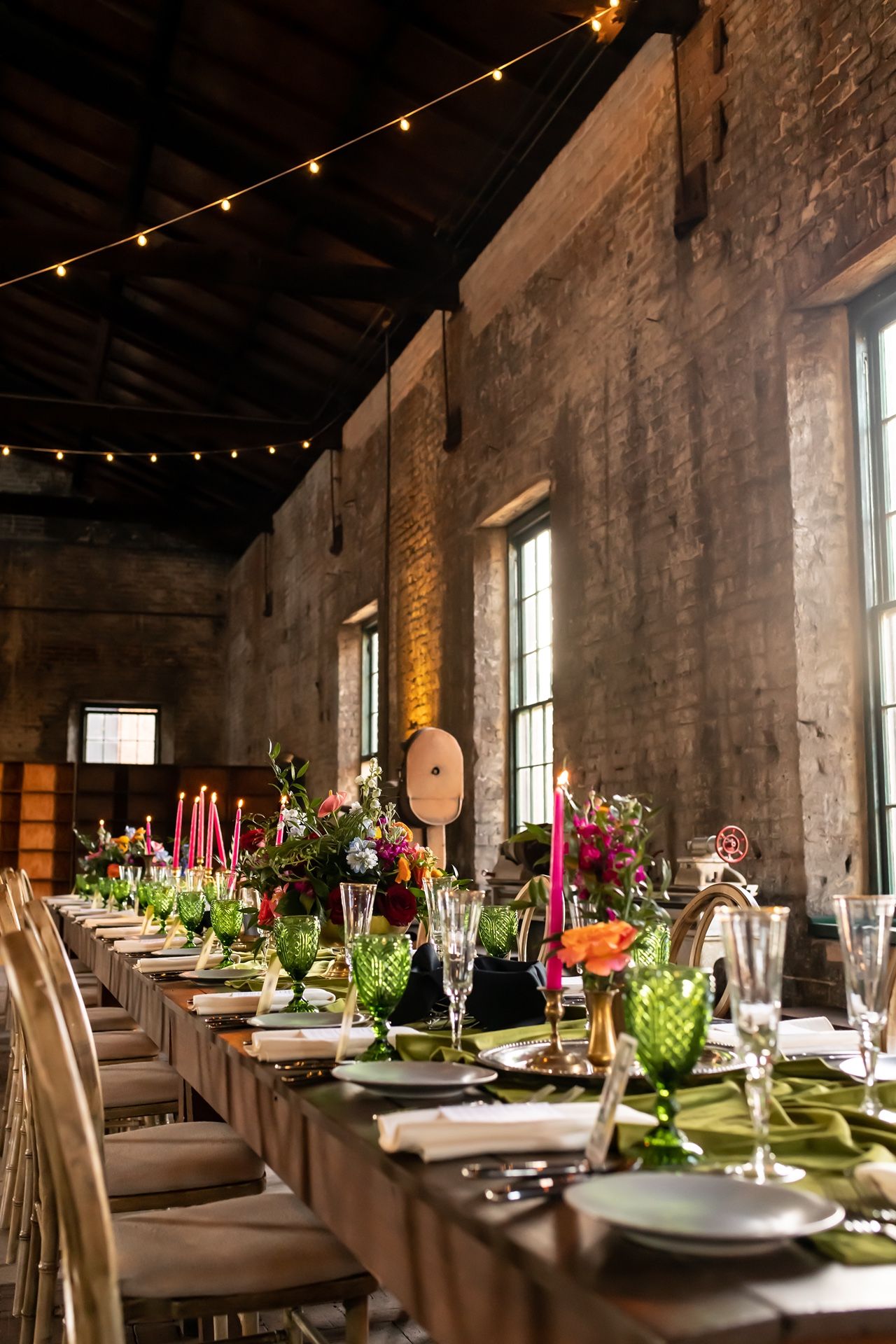 Rustic brick venue decorated with string lights and long banquet tables set for an elegant dinner reception.