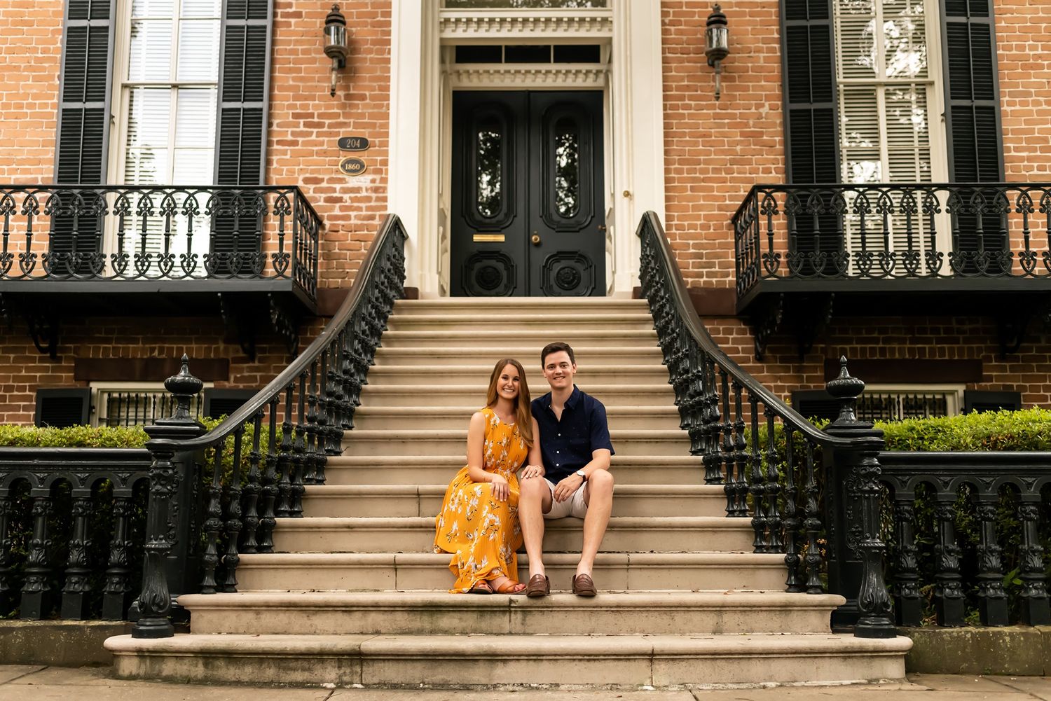 Two people sitting together on grand brick brownstone steps in a historic neighborhood lined with iron railings.