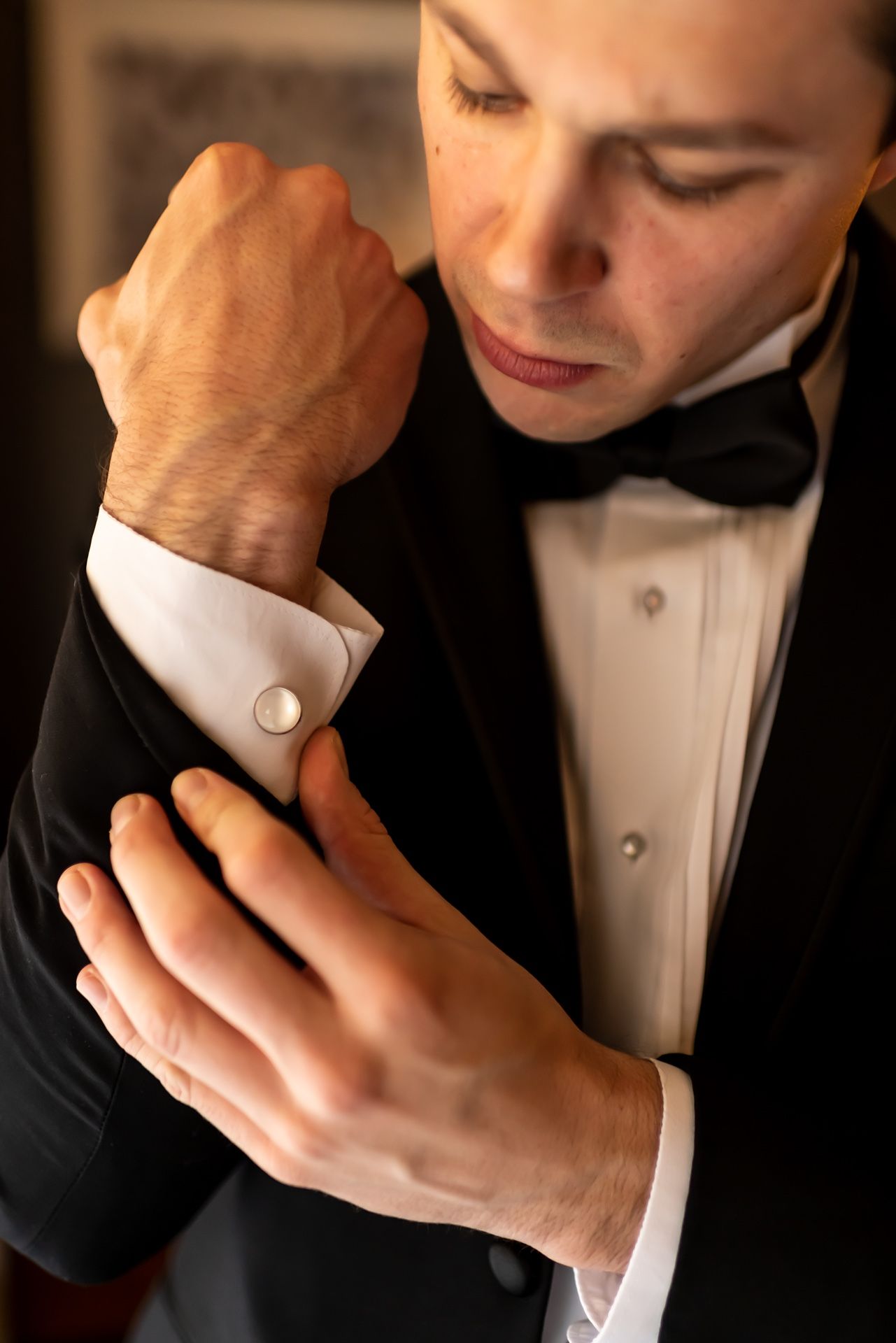 Close-up view of hands adjusting a pearl cufflink on a black tuxedo sleeve with white dress shirt.