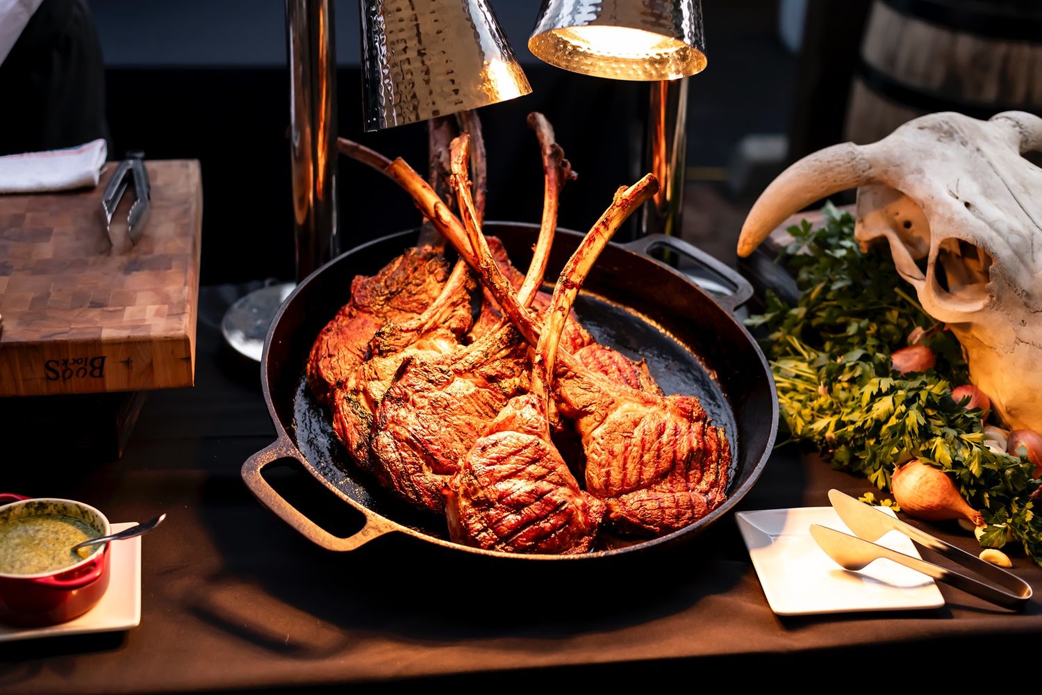 Variety of juicy steaks and meat dishes cooking in cast iron skillets under warm lighting in rustic setting.