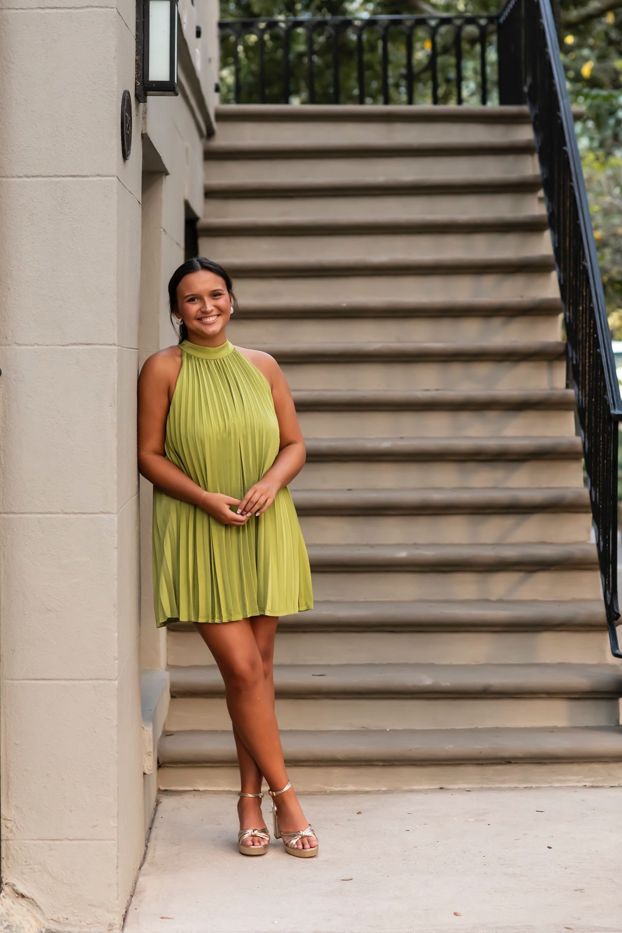 A stylish person in a pleated chartreuse halter dress poses confidently on concrete steps near a railing.