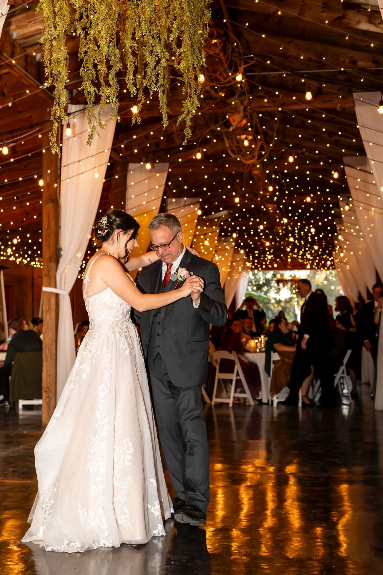 Couple shares a romantic dance under twinkling lights at a rustic barn wedding reception.